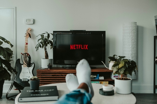 A person watches Netflix with their feet up on a coffee table, wearing white socks